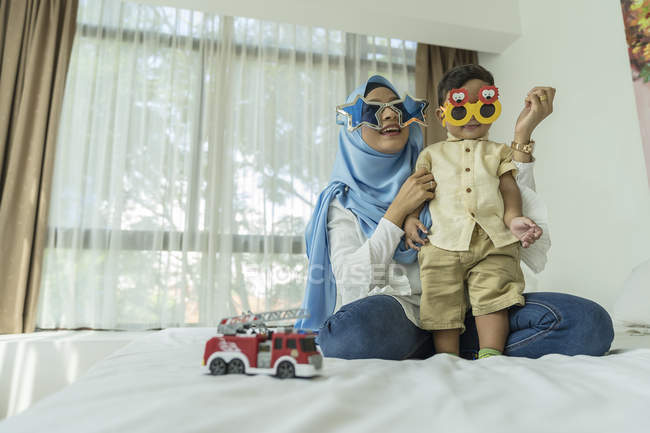 Молодая азиатская мусульманка мать и ребенок в солнечных очках веселятся дома — стоковое фото