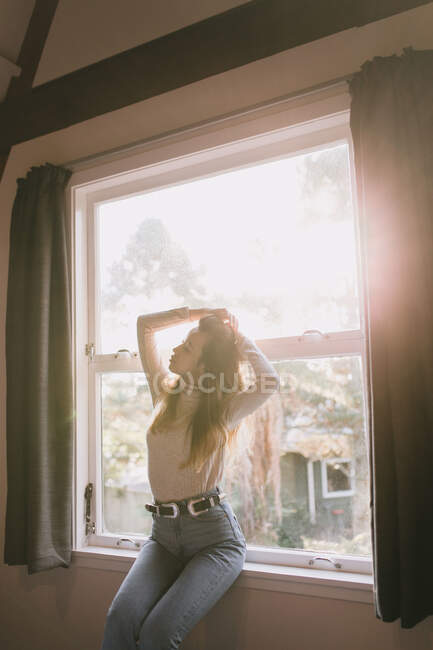 Jovem mulher tomando banho de sol pela janela em sua casa em Queenstown, Nova Zelândia — Fotografia de Stock