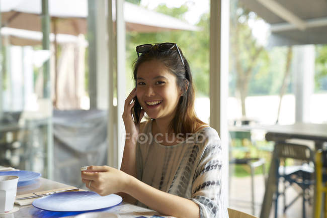Young pretty asian woman talking on smartphone in cafe — Stock Photo