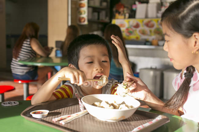 Dos feliz joven asiático niños comer en café - foto de stock