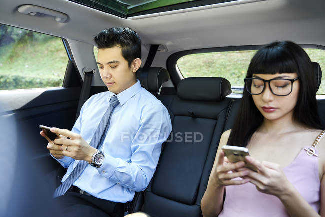 Молода азіатська приваблива пара на мобільних телефонах в машині — стокове фото