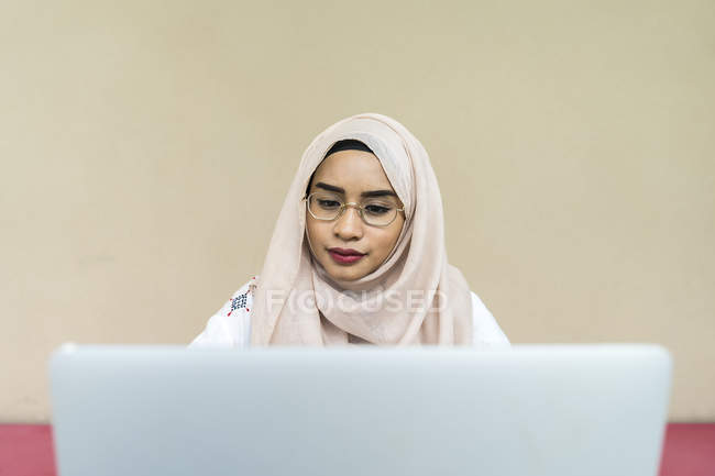 Молода азіатська мусульманка використовує ноутбук у приміщенні — стокове фото
