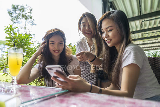 Drei asiatische Mädchen, die gemeinsam im Café auf das Smartphone schauen — Stockfoto