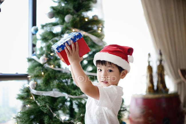 Felice ragazzo asiatico celebrando il Natale e tenendo regalo a casa — Foto stock