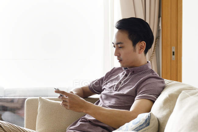Adult asian man using smartphone at home — Stock Photo