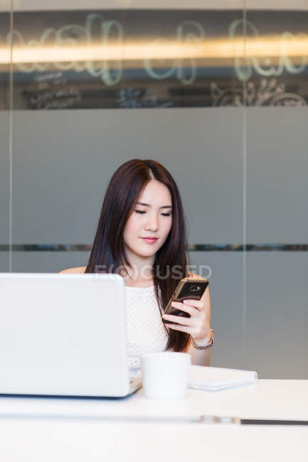 Giovane bella donna asiatica che lavora con laptop e smartphone in ufficio moderno — Foto stock