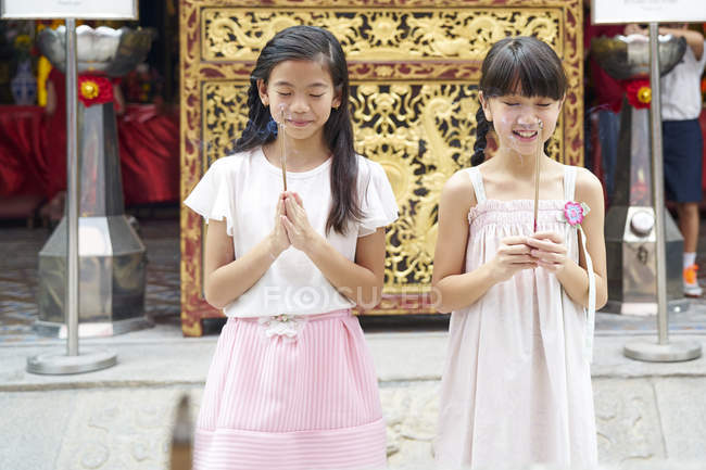Feliz asiático hermanas orando juntos en tradicional singapurense santuario - foto de stock