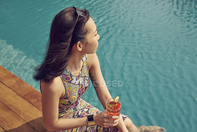 Bela jovem mulher relaxante com bebida perto da piscina — Fotografia de Stock