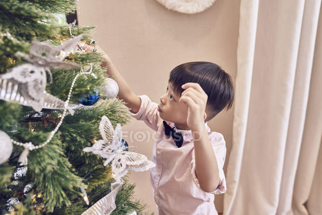 Little asian boy decorating fir tree — Stock Photo