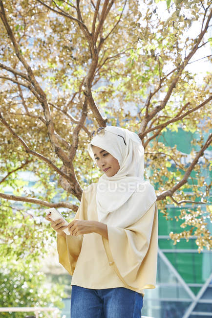 Красивая малайская женщина в хиджабе в парке на мобильном телефоне — стоковое фото