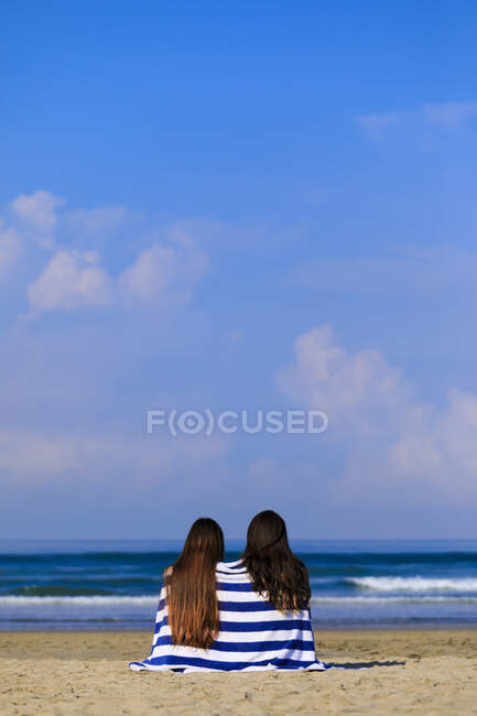 Zwei Freundinnen mit langen Haaren sitzen an einem Strand und genießen den Meerblick.. — Stockfoto