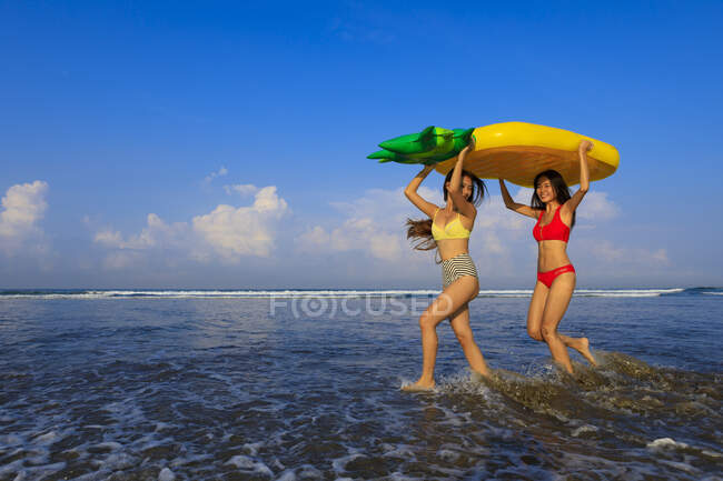 Zwei hübsche Mädchen mit Schwimmwesten auf dem Weg zu den Wellen des Ozeans. — Stockfoto