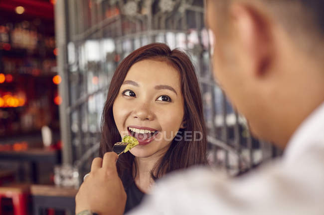 Молода приваблива азіатська пара зустрічається в кафе, чоловік годує жінку — стокове фото