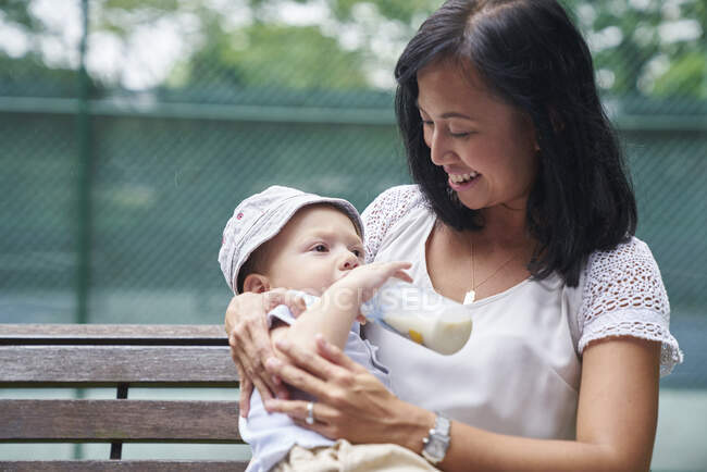 Mãe alimentando filho uma garrafa de leite em um parque em Cingapura — Fotografia de Stock