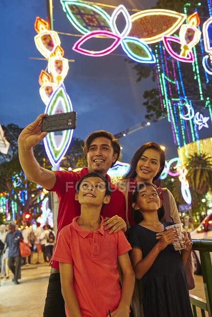 LIBERTAS Familia alegre tomando selfies en Hari Raya Geylang Bazaar, Singapur - foto de stock