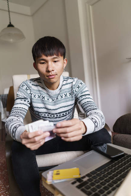 Молодий дорослий азіатський чоловік рахує готівку вдома — стокове фото