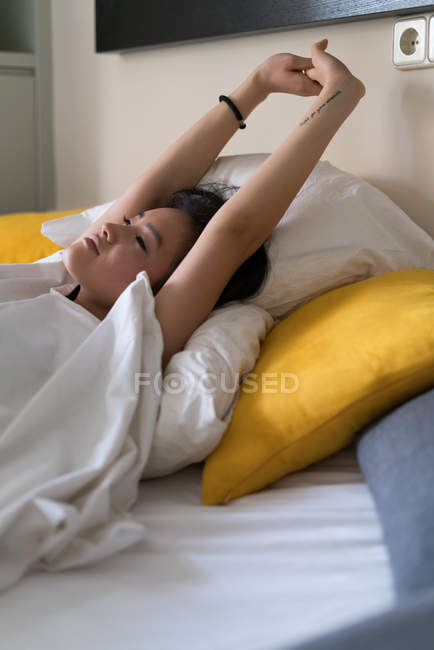 Chinês jovem e bela mulher esticando-se depois de acordar na cama — Fotografia de Stock