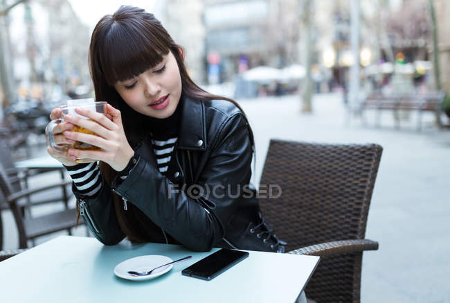 Молода приваблива азіатська жінка має чай у вуличному кафе — стокове фото
