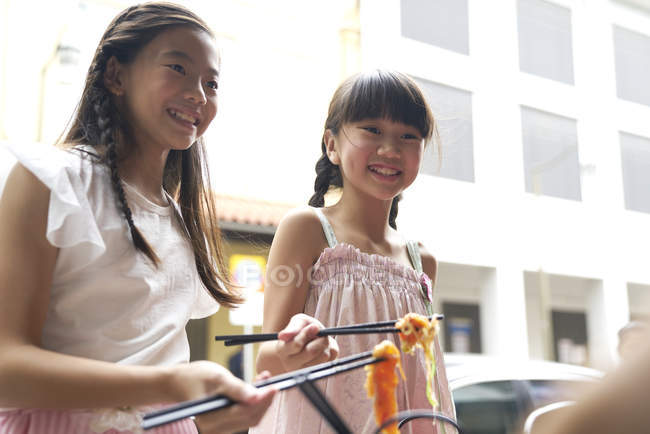 Zwei junge asiatische Schwestern essen Nudeln mit Stäbchen — Stockfoto