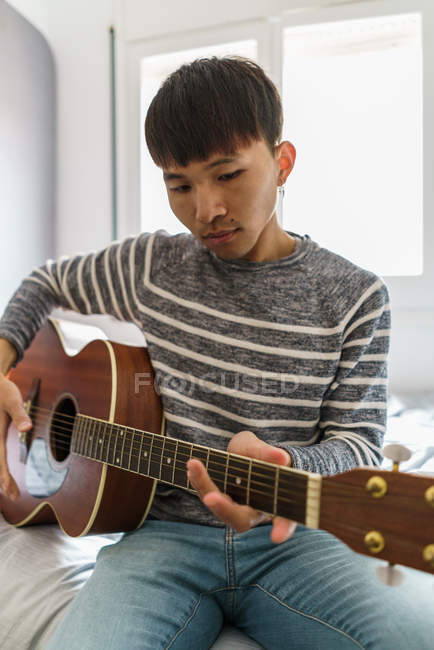 Молодий дорослий азіатський чоловік грає на гітарі вдома — стокове фото