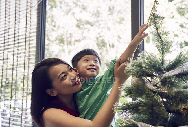 Happy young asian mother and son celebrating christmas together and decorating fir tree — Stock Photo