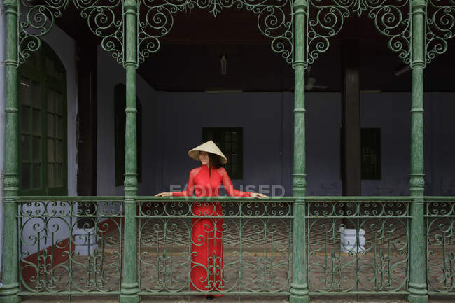 Вьетнамская женщина в конической шляпе, стоящая на балконе в Хой Ане в своем Ао Дай — стоковое фото