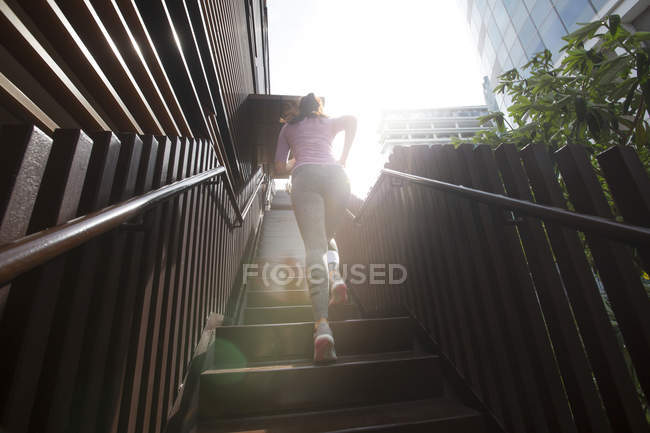 A young asian woman is jogging through the city of Singapore in the early morning. She passes a section of steel and glass architecture. — Stock Photo