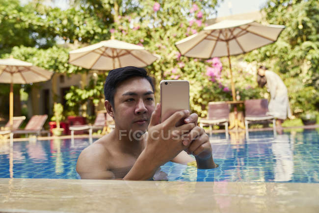 Giovane asiatico uomo utilizzando telefono in piscina — Foto stock