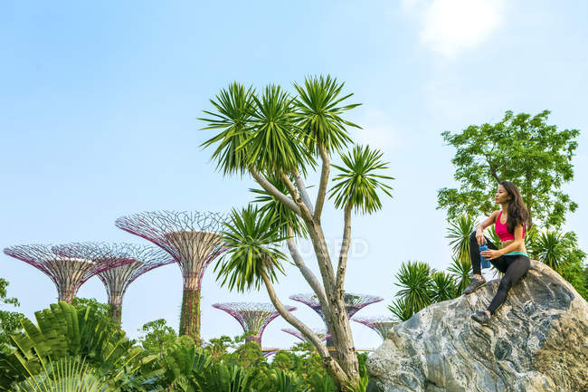 A young singaporean woman is resting at Gardens by the bay from her workout. A water bottle is next to her. — Stock Photo