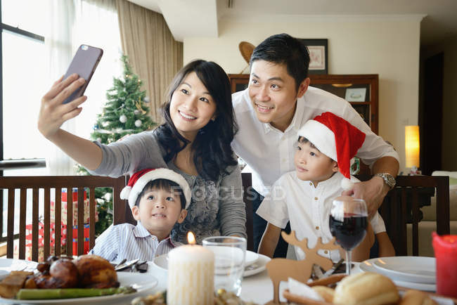 COMMUNIQUÉS Happy Asian family celebrating Christmas together at home and taking selfie — Photo de stock
