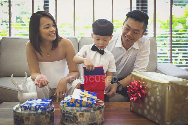 Madre e padre guardando il loro figlio aprire i suoi regali di Natale nella loro casa a Singapore . — Foto stock
