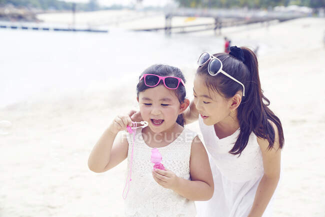 RELEASES Two little sisters spending time together on beach and blowing bubbles — Stock Photo