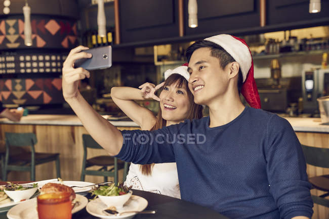 Feliz joven asiático pareja celebrando Navidad juntos en café y tomando selfie - foto de stock