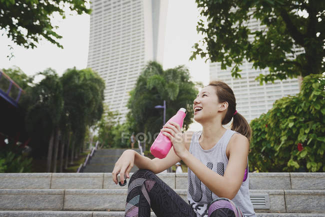 Junge asiatische sportliche Frau trinkt Wasser aus der Flasche — Stockfoto