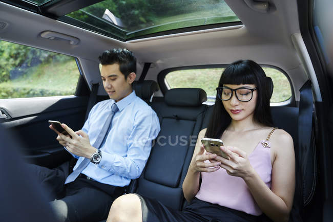 Young asian attractive couple on mobiles in the car — Stock Photo
