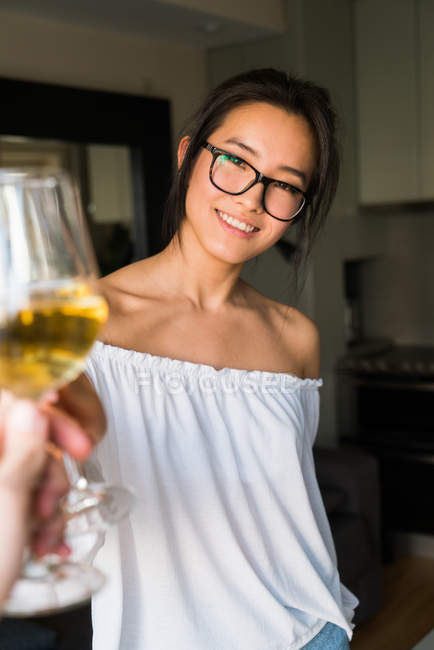 Mujer china tostada con vino blanco sonriendo con copas en el interior - foto de stock