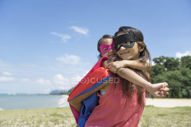 Junge asiatische Mutter mit süßer Tochter im Superheldenkostüm posiert vor blauem Himmel — Stockfoto