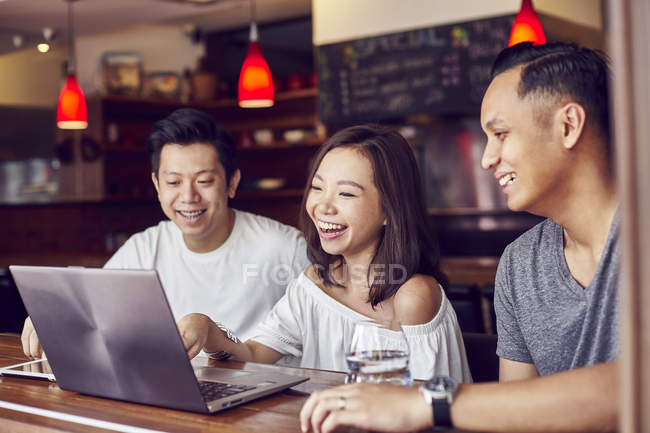Счастливый молодой человек вместе с друзьями работает с ноутбуком в баре — стоковое фото