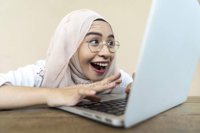 Молода здивована азіатська мусульманка використовує ноутбук у приміщенні — стокове фото