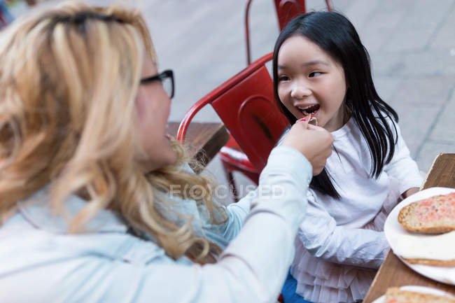 Щаслива молода мати годує свою дочку хлібом з шинкою — стокове фото
