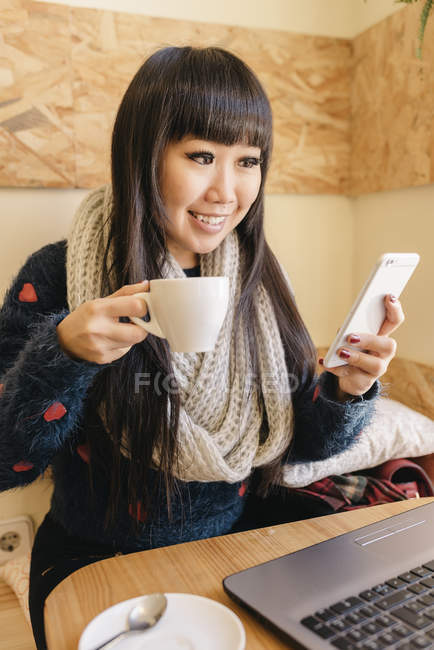 Young attractive asian woman using smartphone in cafe — Stock Photo