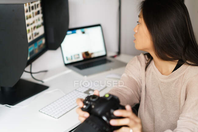 Mujer joven que sostiene su cámara y mira la pantalla del ordenador - foto de stock