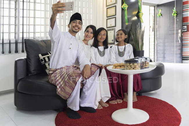 Happy asian family celebrating hari raya at home and taking selfie — Stock Photo