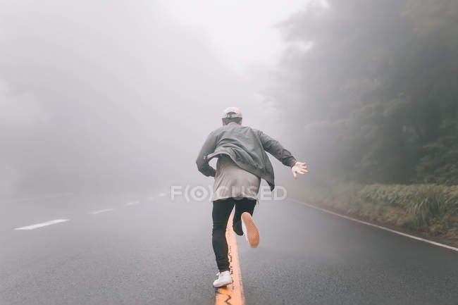 Вид сзади на молодого хипстера, бегущего по дороге в сельской местности Токио — стоковое фото
