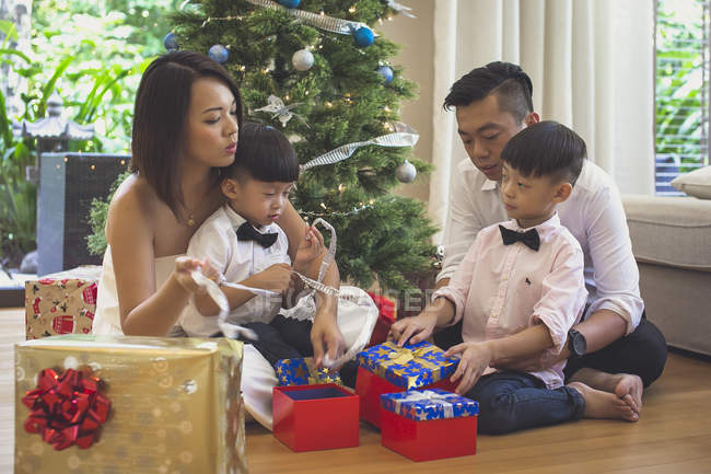 Familia de cuatro personas se sienta en el suelo y abre regalos de Navidad - foto de stock