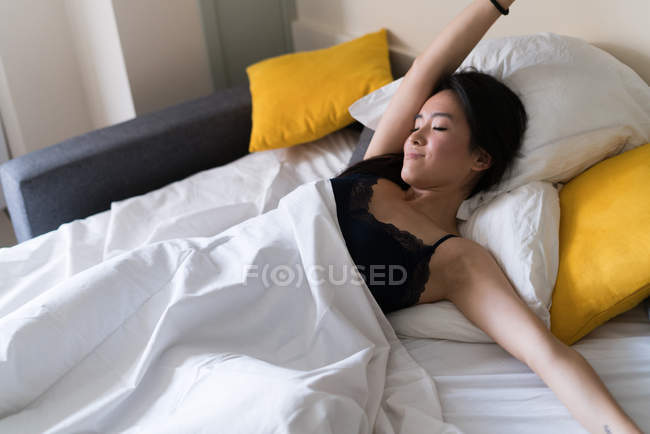Chinoise jeune et belle femme étirant vers le haut après s'être réveillée au lit — Photo de stock