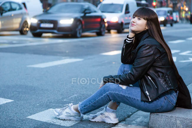 Молода приваблива азіатська жінка в місті сидить біля дороги — стокове фото