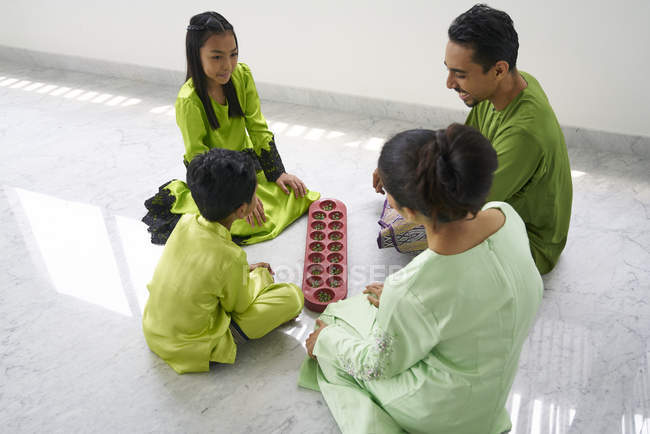 Young asian family celebrating Hari Raya together at home and playing traditional game — Stock Photo