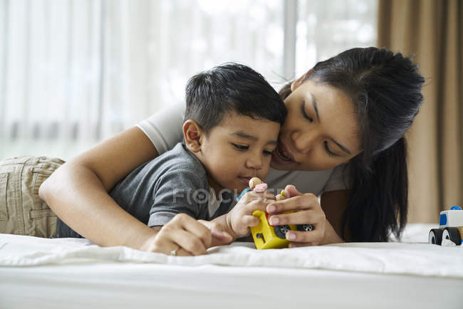 Asiática mãe e filho brincando com brinquedos na cama — Fotografia de Stock