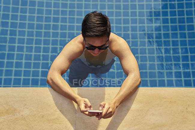 Young man using phone in the pool — Stock Photo